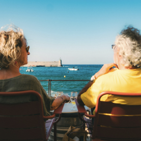 two women sitting on a bench looking out at the ocean